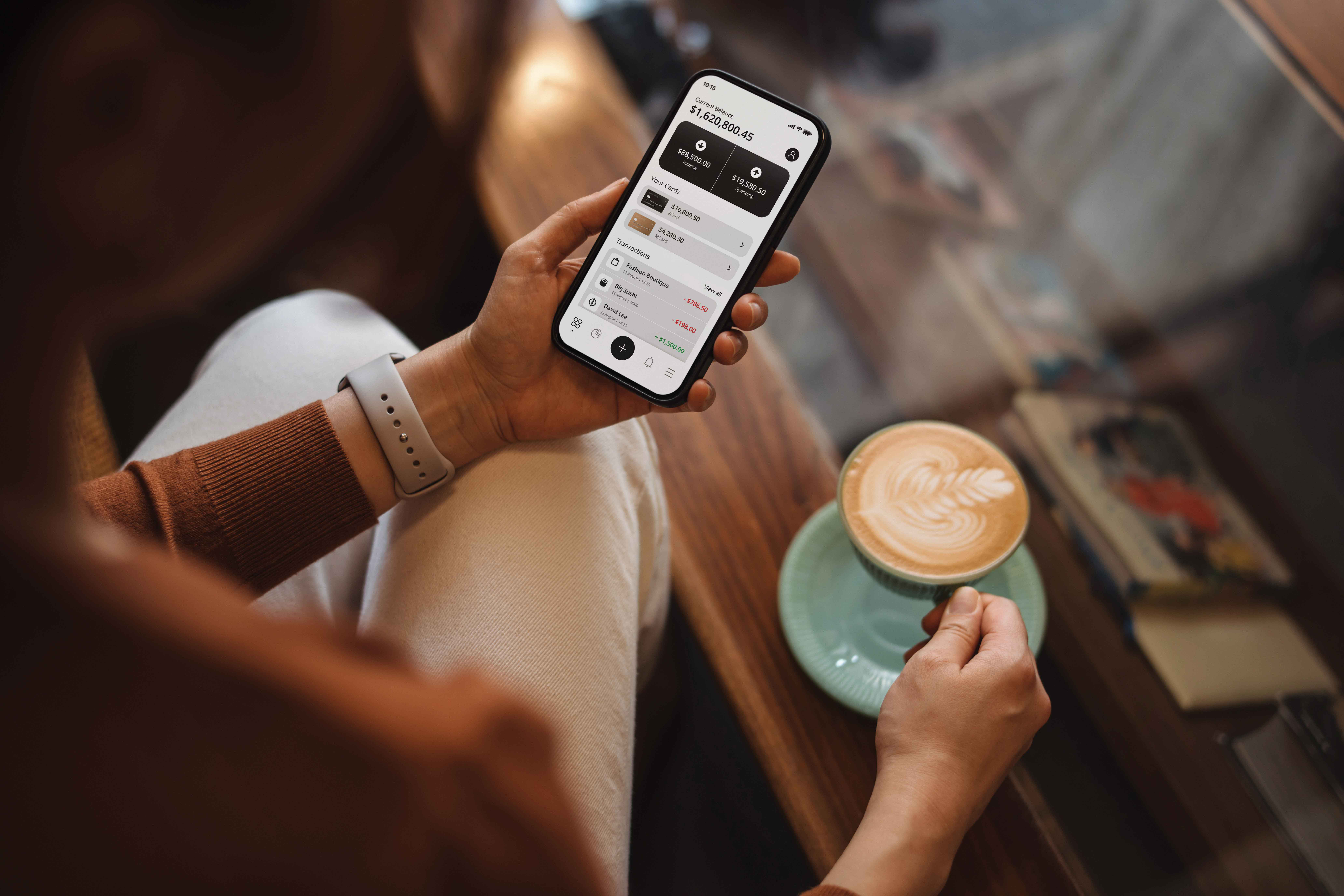 Photo that shows a woman on iPhone reviewing expenses while drinking a cappuccino